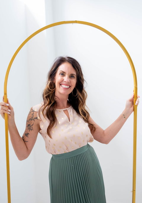 Julie Bowman standing inside a gold arch, both hands on the frame, smiling directly at the camera.