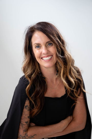 Julie Bowman in a black cape blazer, arms relaxed, smiling directly at the camera.